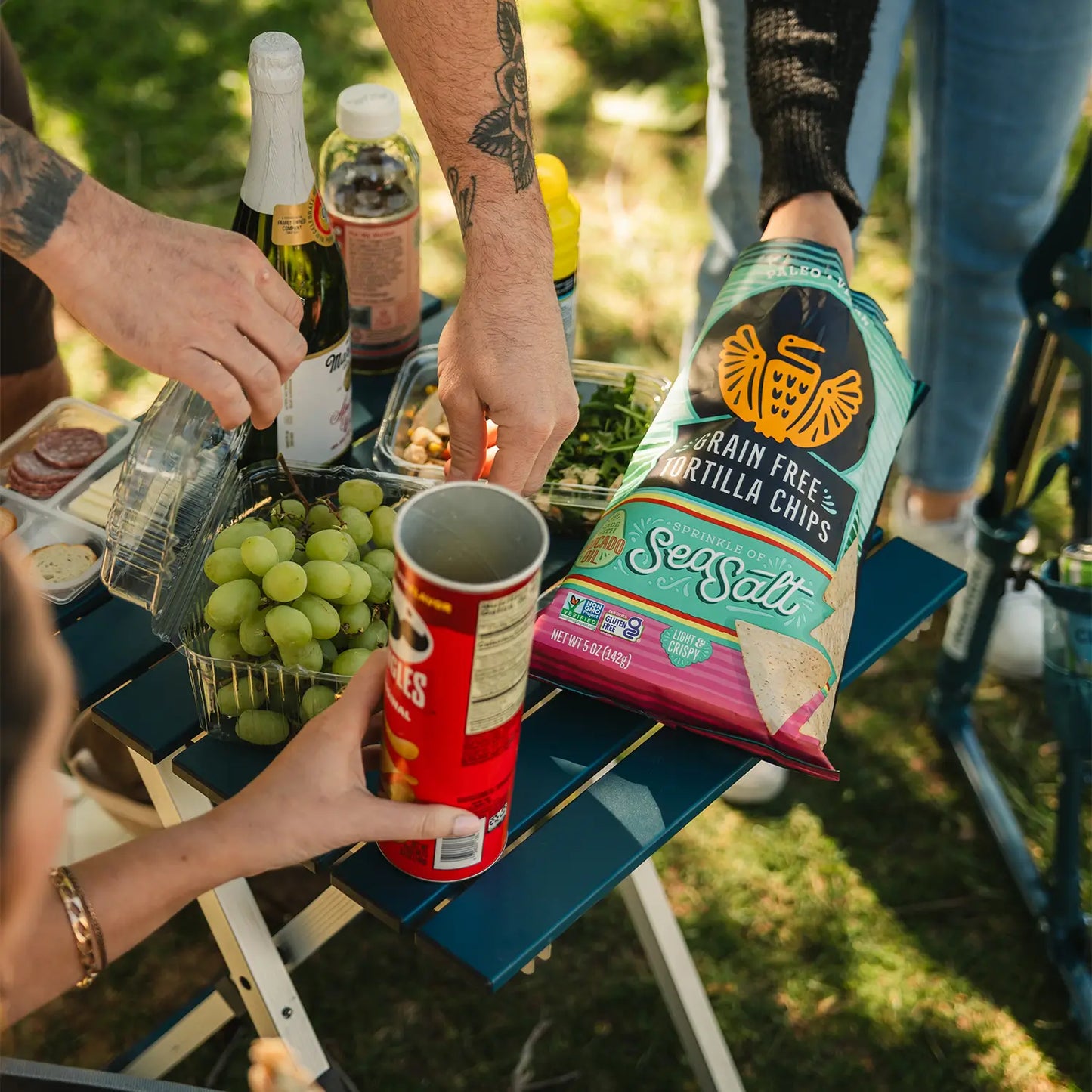 A group of people reaching for snacks positioned on top of a teal Compact Camp Table. 