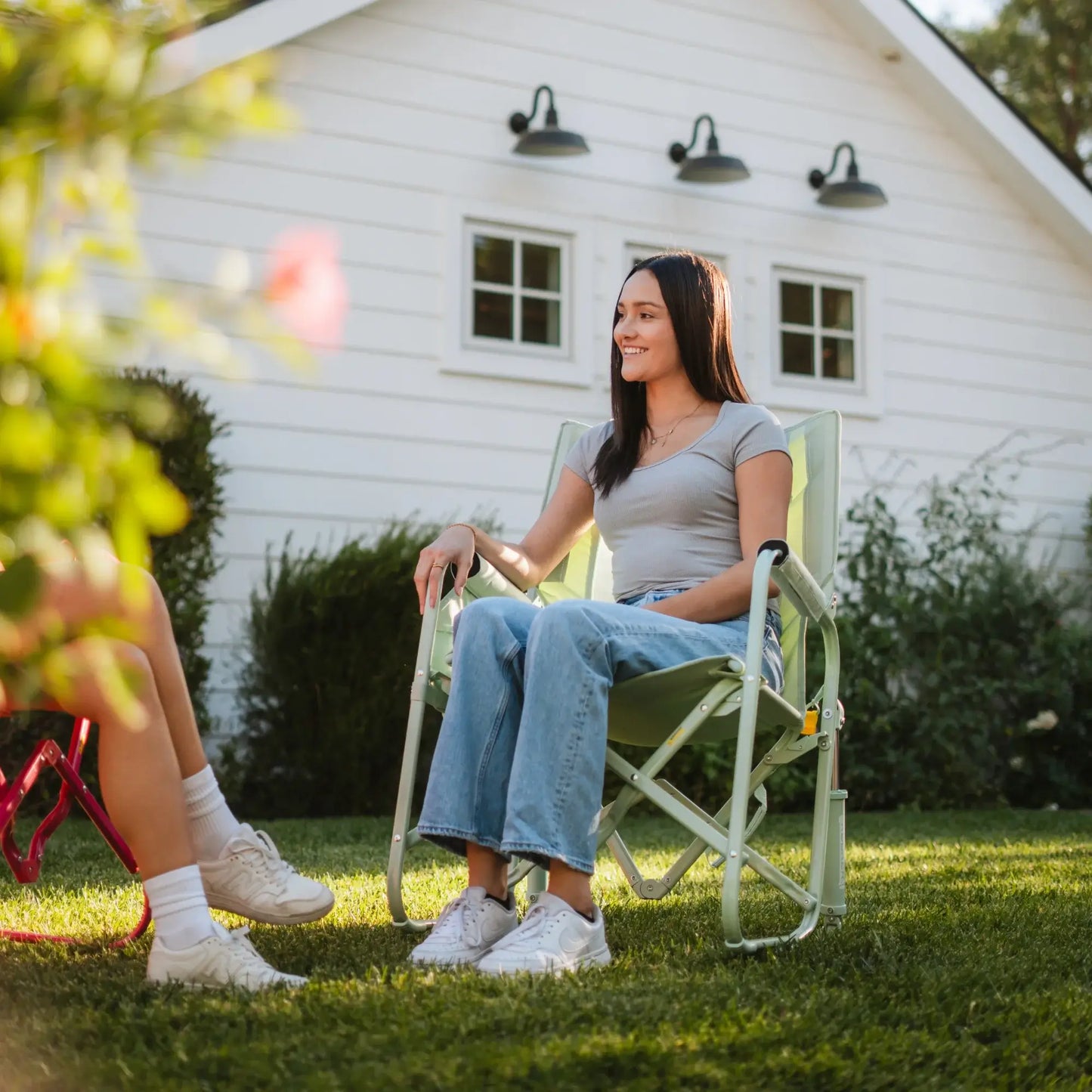 A woman sitting in a pastel green Stowaway Rocker in a backyard setting. 