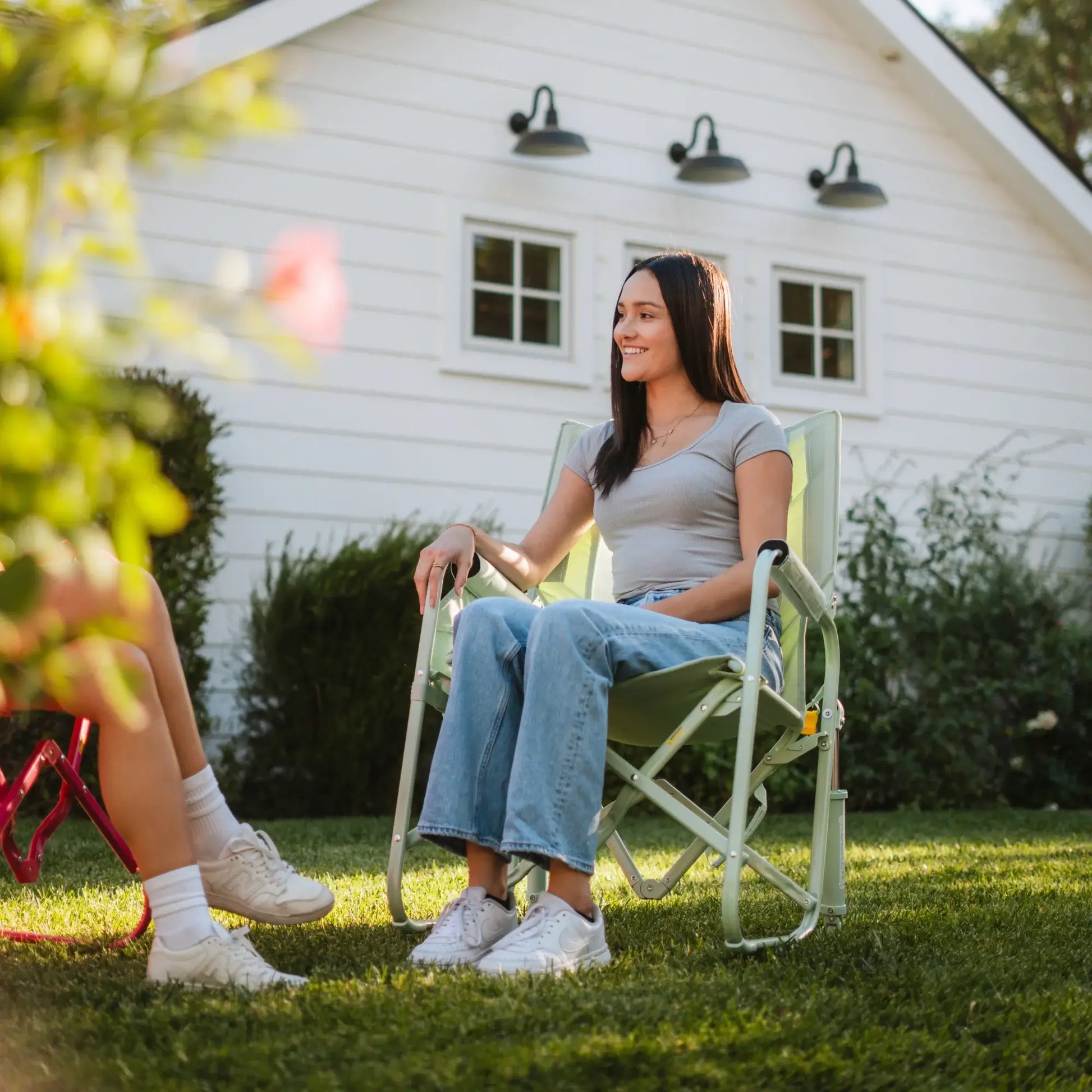 A woman sitting in a pastel green Stowaway Rocker in a backyard setting. 