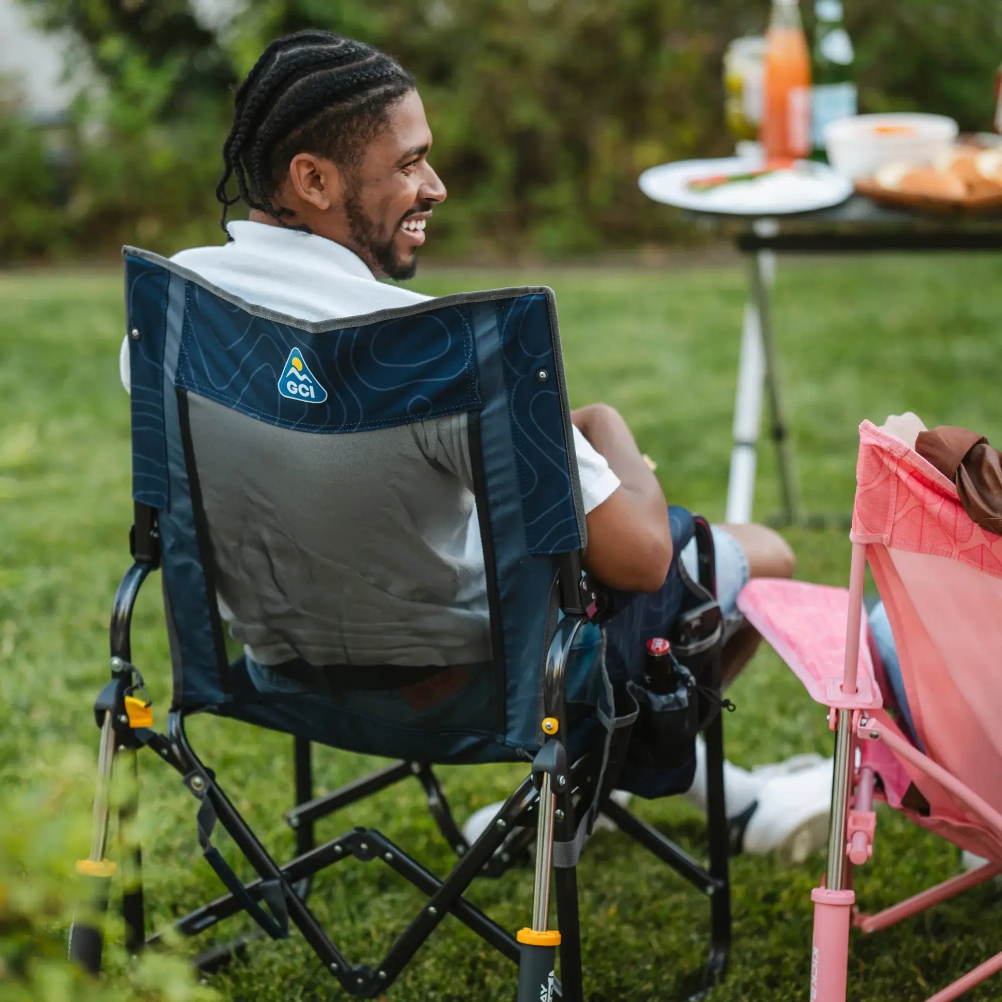 A man laughing and talking with a person while sitting in a navy topo Stowaway Rocker in a backyard setting. 