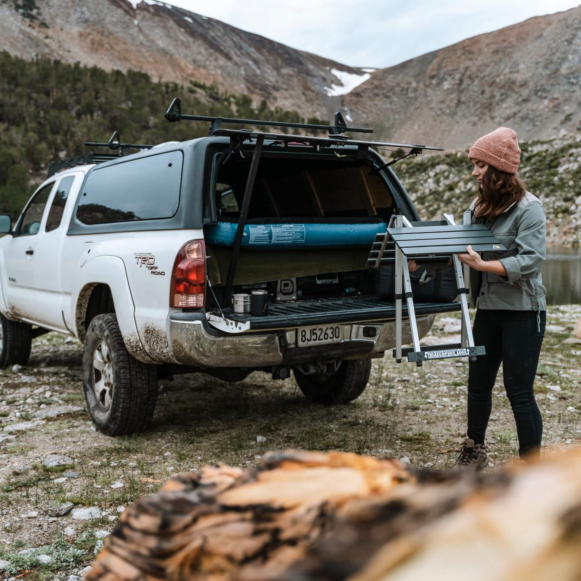 A woman unfolding the compact camp table 20 from her trucks tailgate. 
