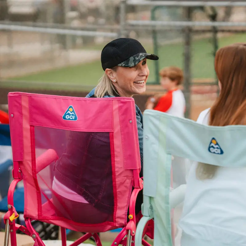 Woman smiling while seated in the bright pink Stowaway Rocker beside others at a sports field.
