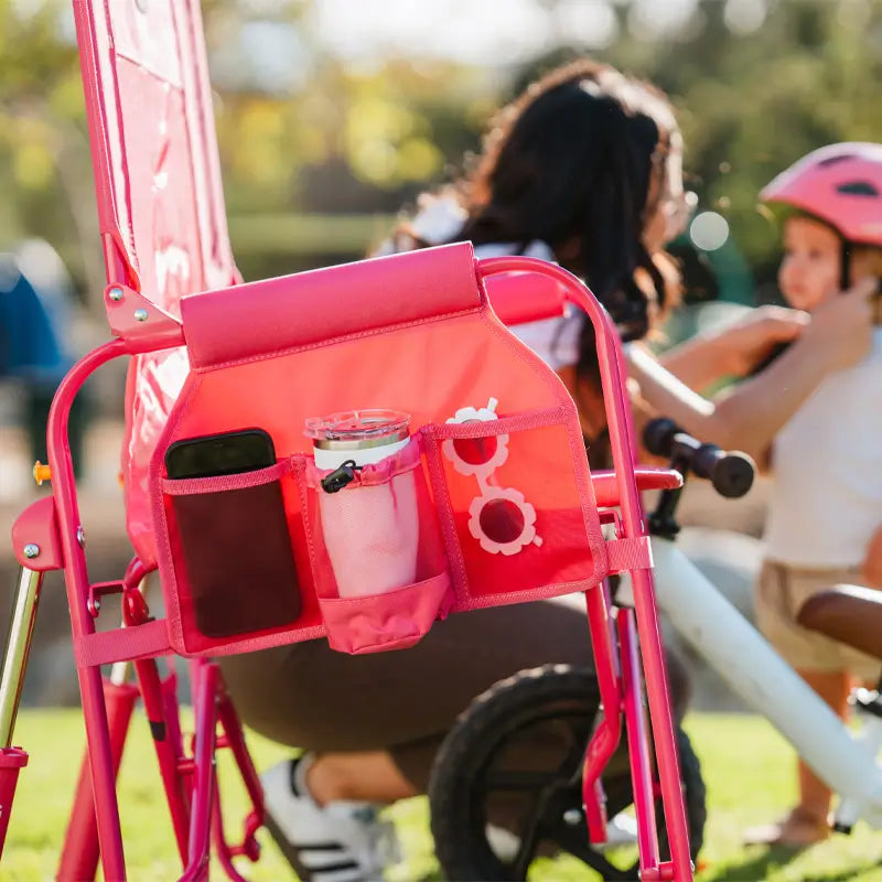 Bright pink Stowaway Rocker with a loaded storage pocket, while a child is helped with a helmet nearby.