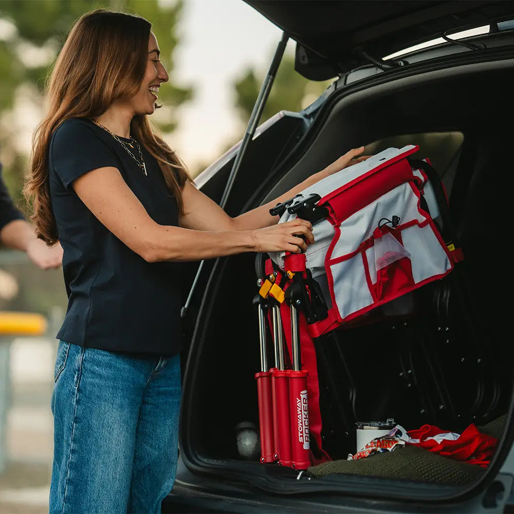 A woman loading up her folded stowaway rocker baseball print into her car. 